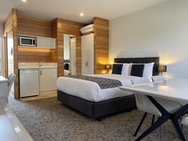 Una habitación de hotel moderna con cama, mesita de noche, escritorio y una pequeña cocina.