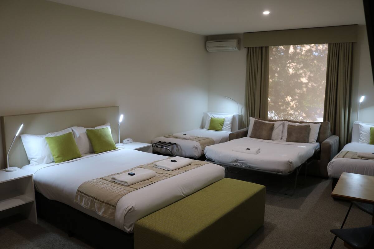 A hotel room with two single beds, a sofa, a small table, and a desk with a lamp.