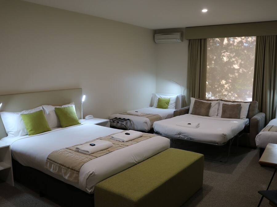 Habitación de hotel con dos camas individuales, un sofá, una mesita y un escritorio con lámpara.