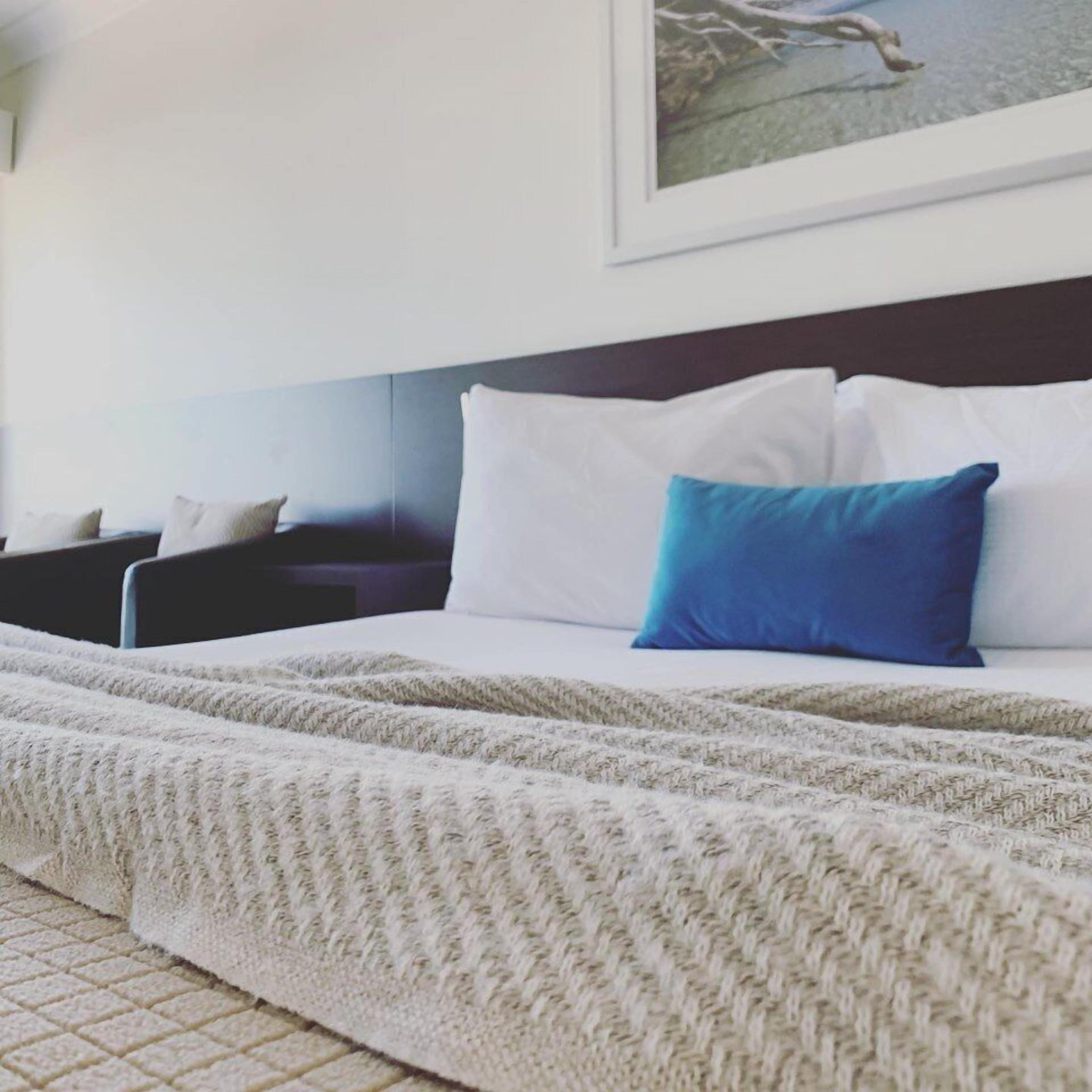 A neatly made bed with white and blue pillows, a white blanket, and a headboard.