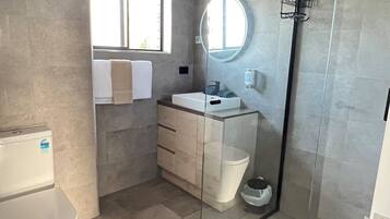 Un baño moderno con ducha envuelta en vidrio, inodoro, lavabo con espejo y ventana que deja entrar luz natural.