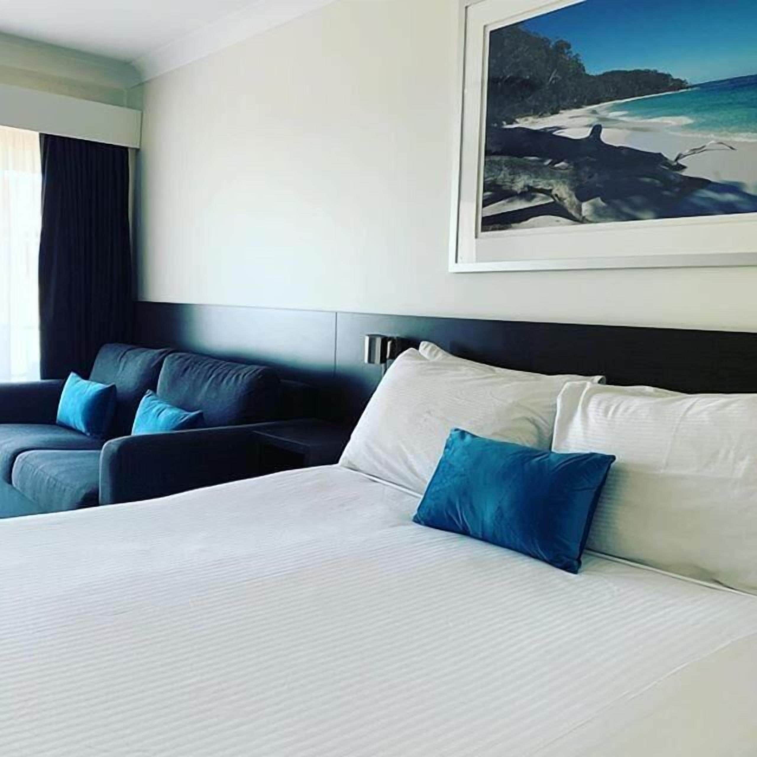 Une chambre d’hôtel avec un grand lit, deux fauteuils et un tableau représentant une scène de plage.