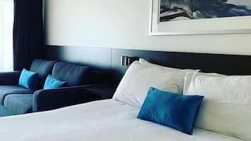 Une chambre d’hôtel avec un grand lit, deux fauteuils et un tableau représentant une scène de plage.