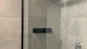 Een moderne douche met glazen scherm, een handdouche en bediening aan de muur.