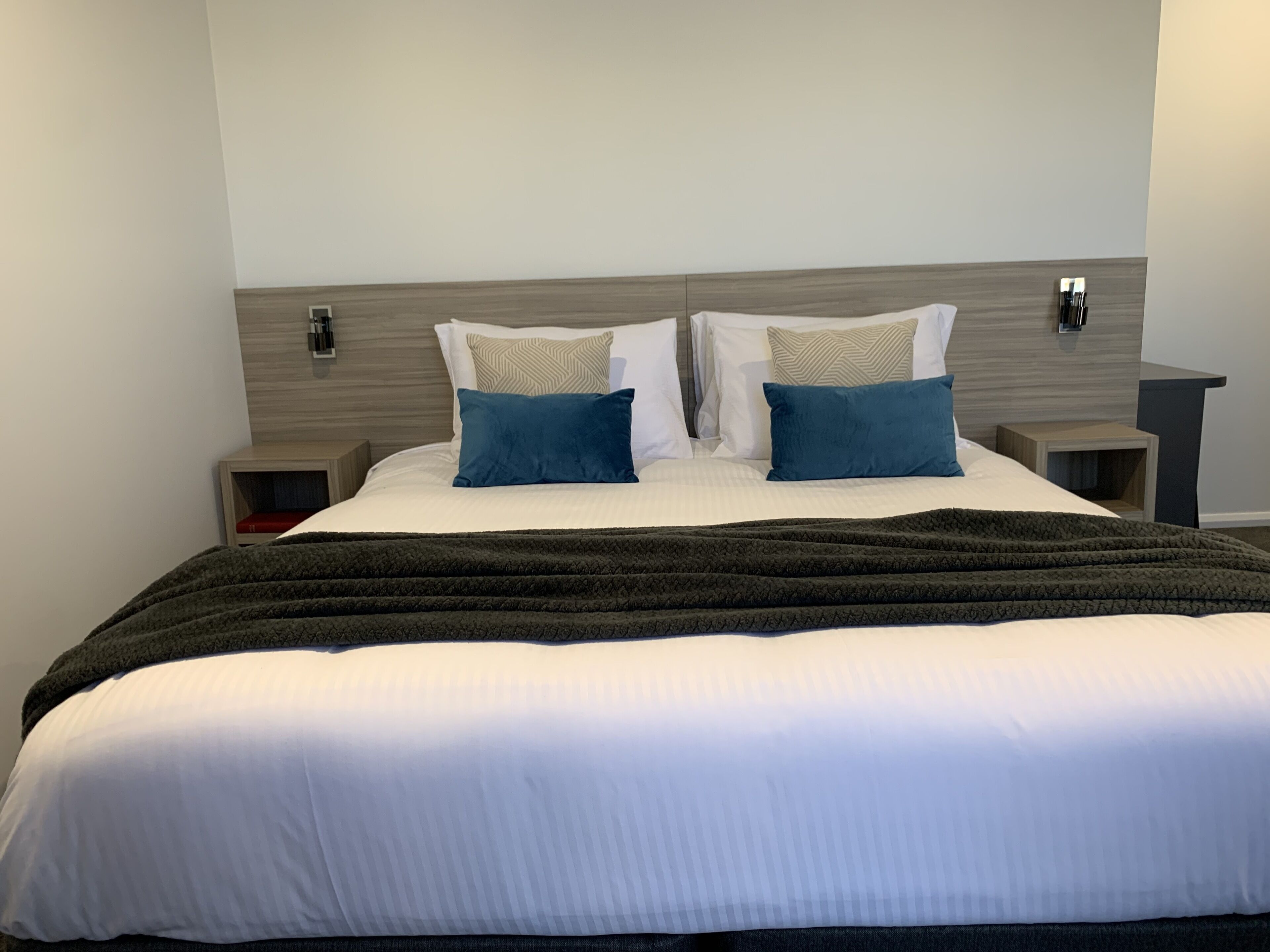 A neatly made bed with a dark blanket, two bedside tables with lamps, and a light-colored headboard.