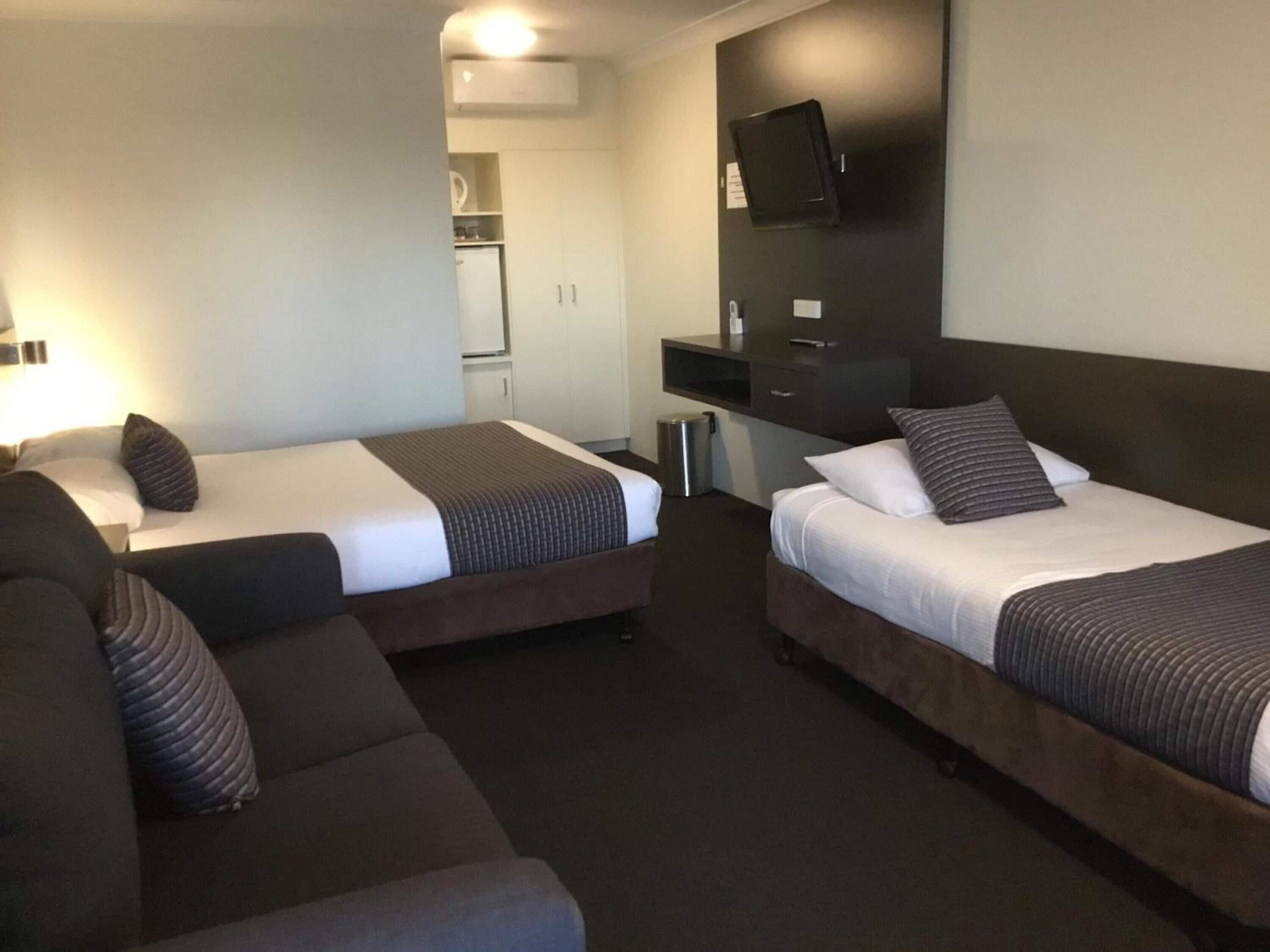 A hotel room with two single beds, a sofa, a desk, and a TV.