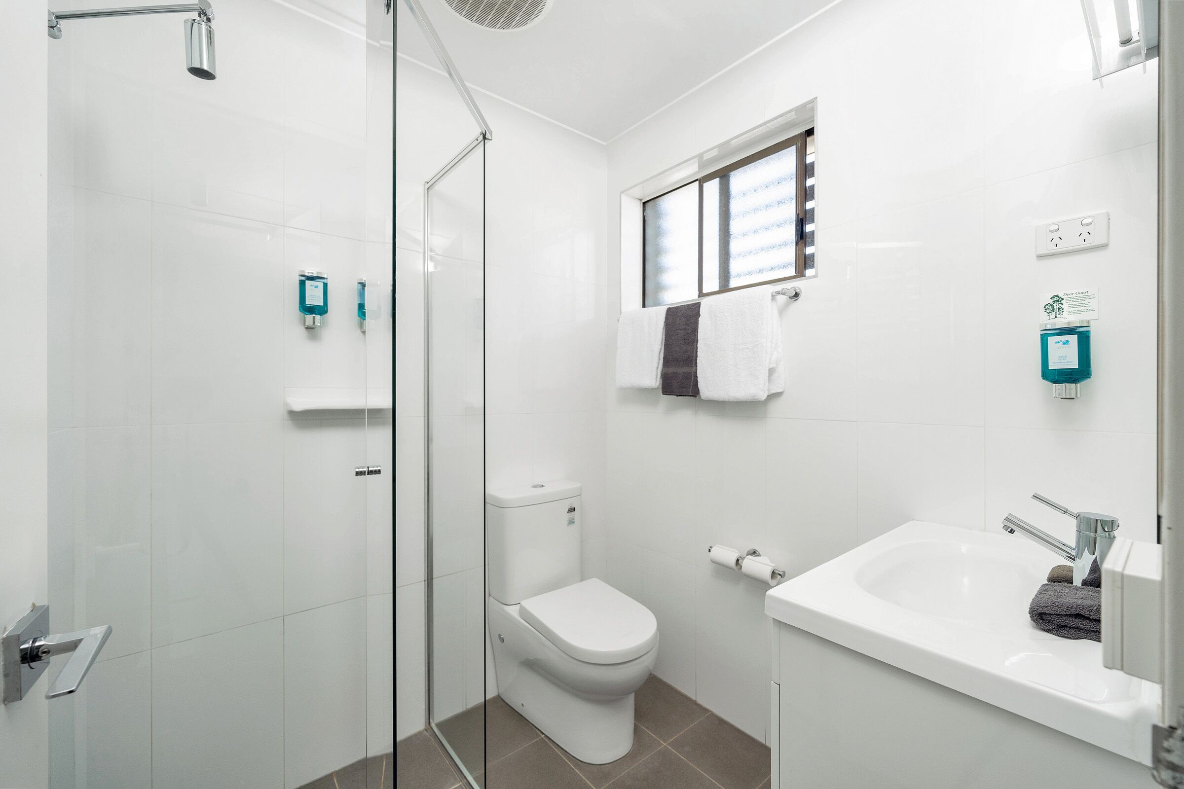 A modern bathroom with a glass shower enclosure, a white toilet, a sink with a mirror, and a window providing natural light.