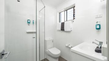 A modern bathroom with a glass shower enclosure, a white toilet, a sink with a mirror, and a window providing natural light.