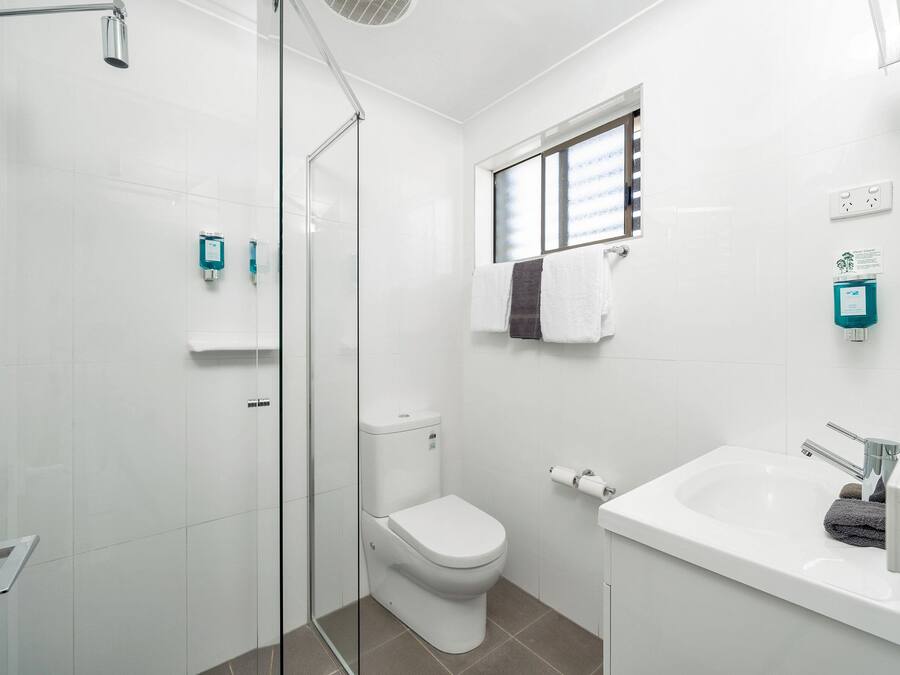 A modern bathroom with a glass shower enclosure, a white toilet, a sink with a mirror, and a window providing natural light.