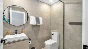 A modern bathroom with a glass-enclosed shower, a white sink with toiletries, and a toilet.