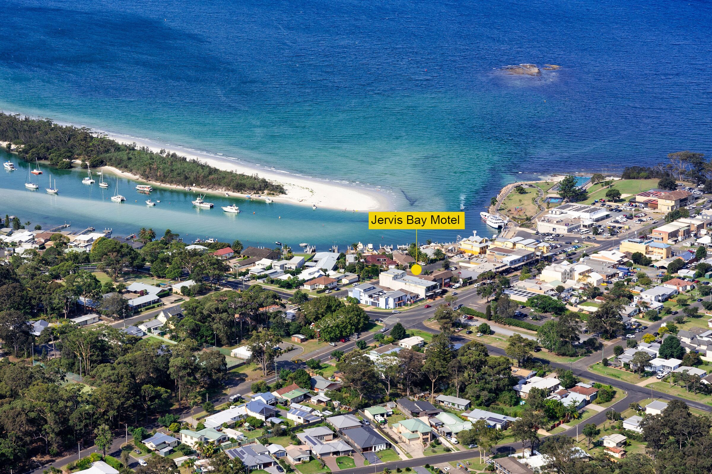 Vista aérea del Motel Jervis Bay, con acceso directo a la playa, zona residencial aledaña y aguas azules cristalinas.