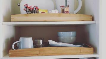 A kitchen with a white refrigerator, a coffee maker, a kettle, and various kitchen utensils on wooden shelves.