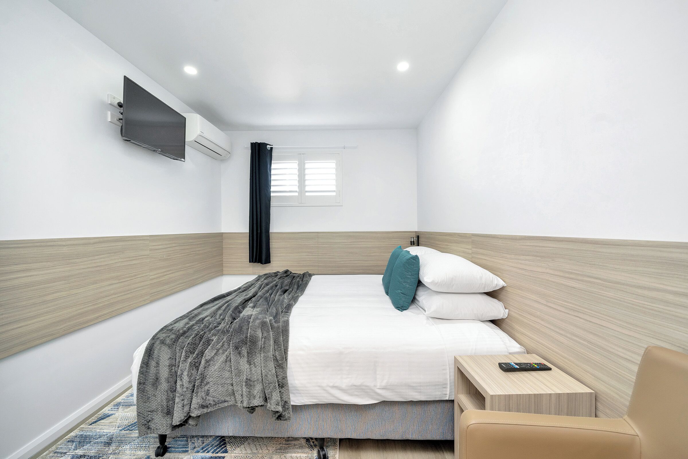 Una habitación de hotel moderna con una cama, una mesita de noche y un televisor montado en la pared.