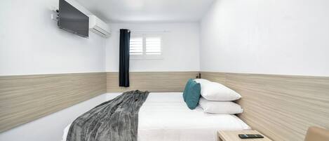 Ein modernes Hotelzimmer mit Bett, Nachttisch und an der Wand montiertem Fernseher.