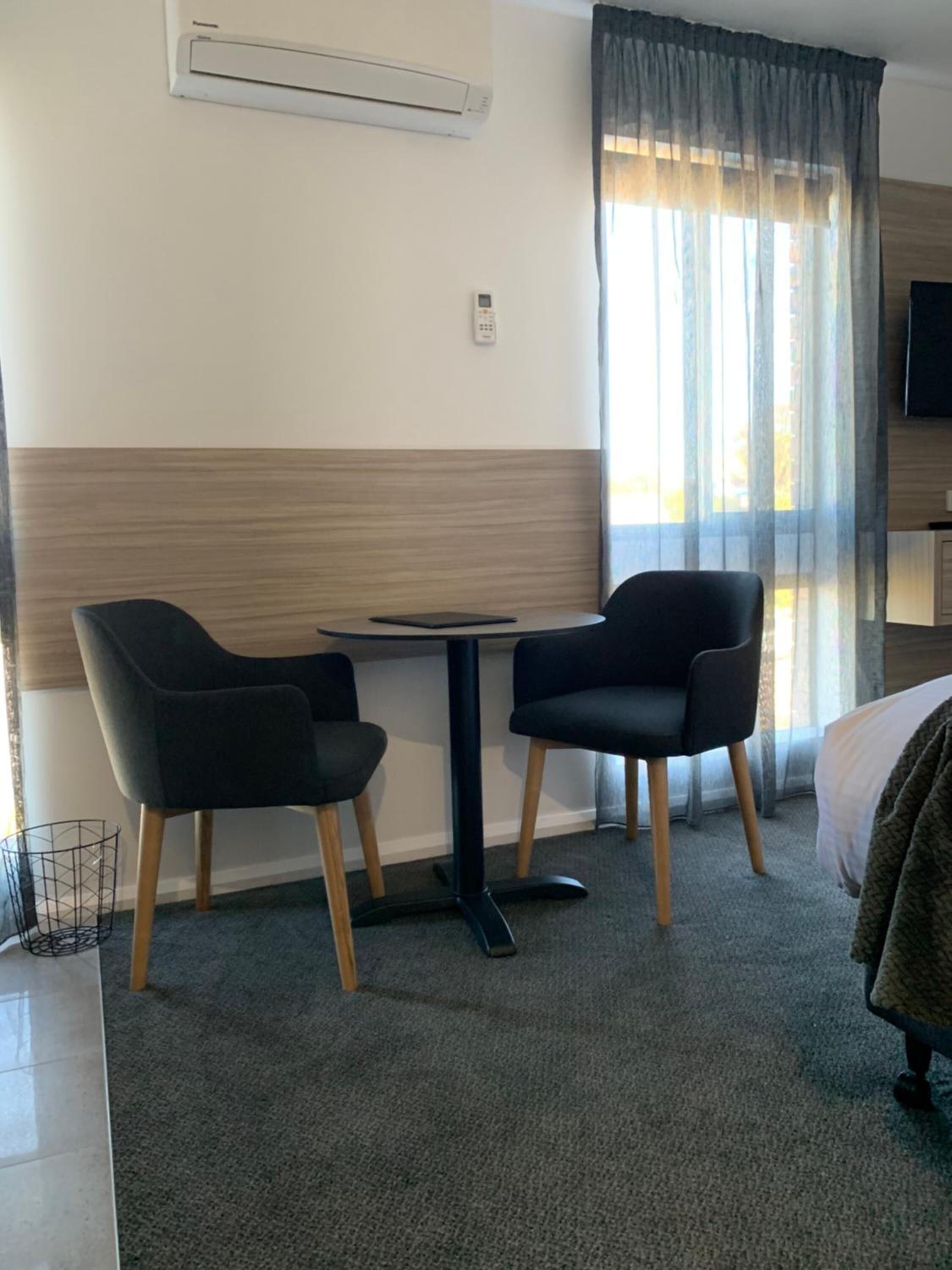 Habitación de hotel con cama, una mesita con dos sillas, un equipo de aire acondicionado y ventana con cortinas.