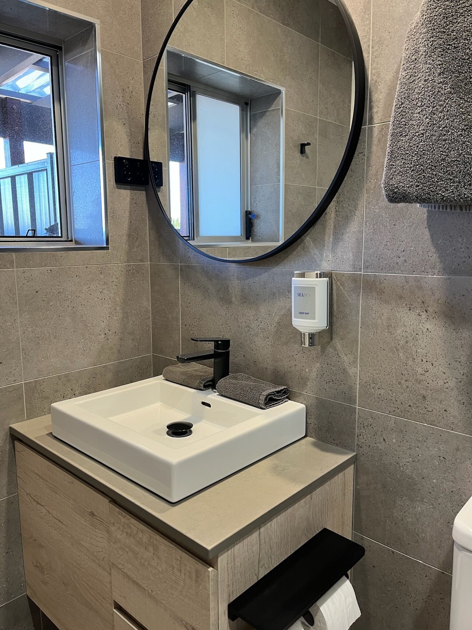 A modern bathroom with a white sink, a round mirror, and a window.