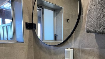 A modern bathroom with a white sink, a round mirror, and a window.