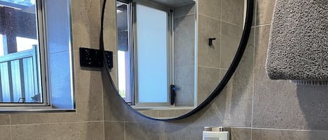 Een moderne badkamer met een wit wastafelmeubel, een ronde spiegel en een raam.