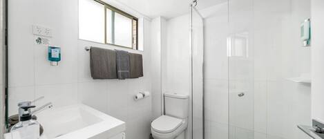 A modern bathroom with a white sink, toilet, and glass shower enclosure.