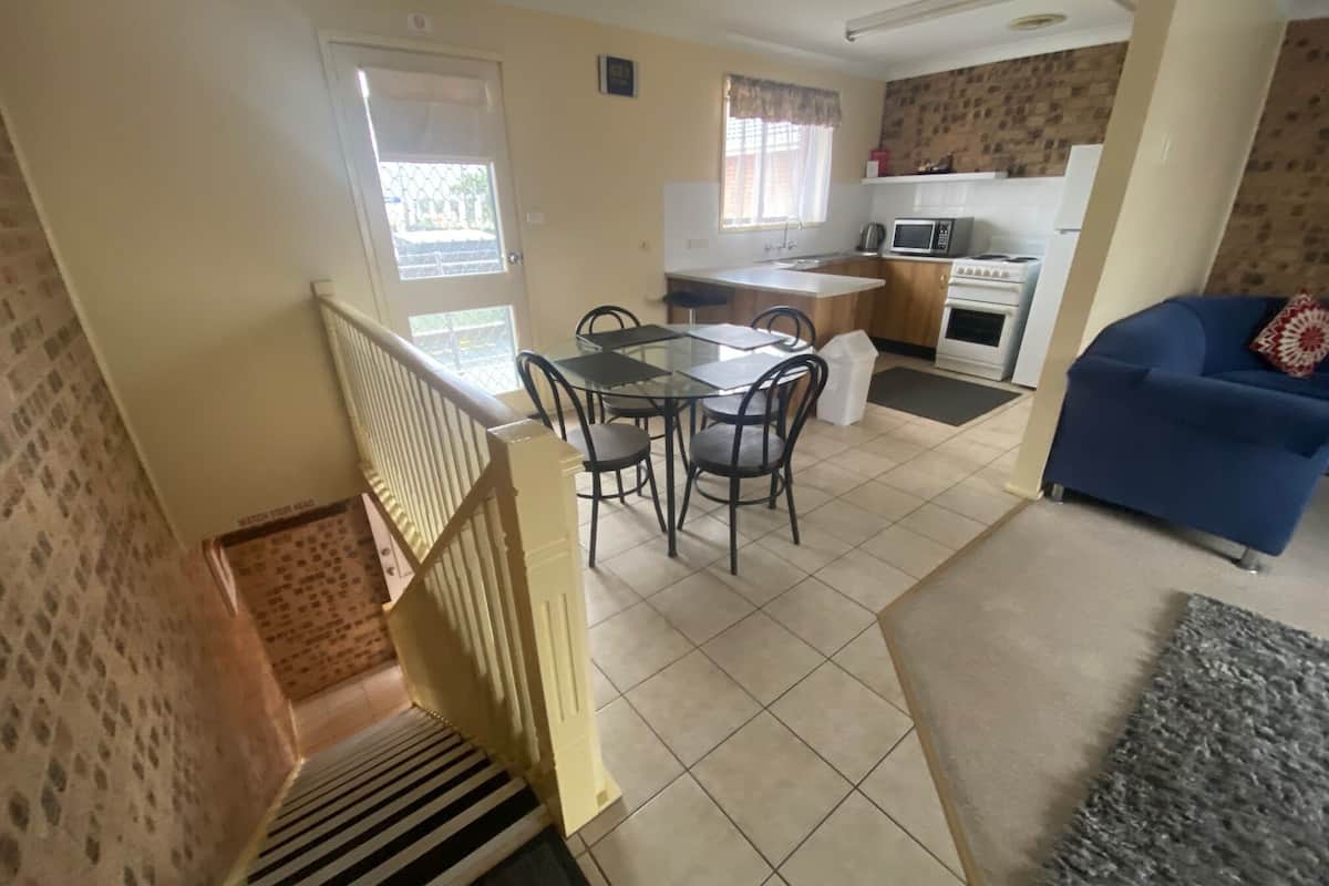 A modern kitchen with a dining area, a staircase, and a living room with a sofa.
