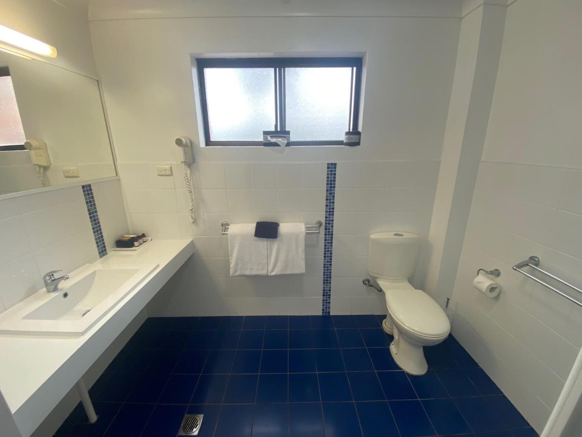 Un baño con lavamanos blanco, inodoro y ventana sobre el inodoro.