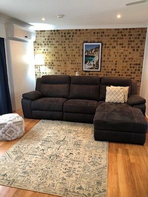 Una sala de estar con un sofá seccional marrón, un tapete estampado y una pared con diseño de ladrillo.
