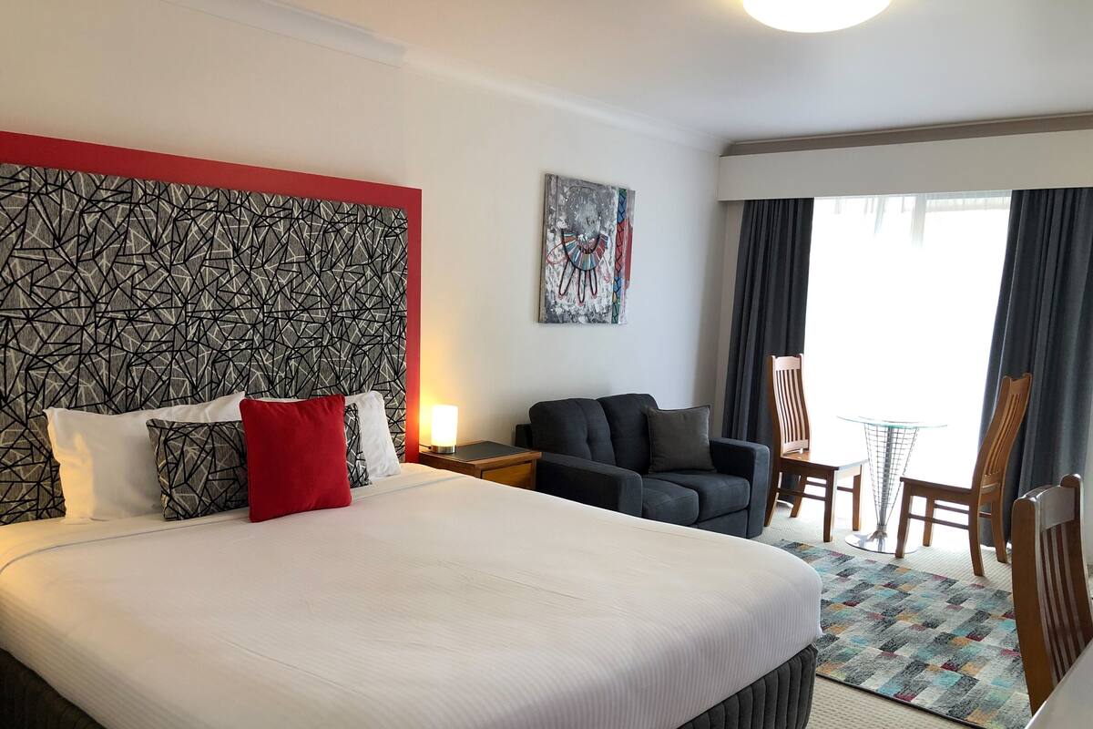 A hotel room with a large bed, a sofa, a small table, and a chair.