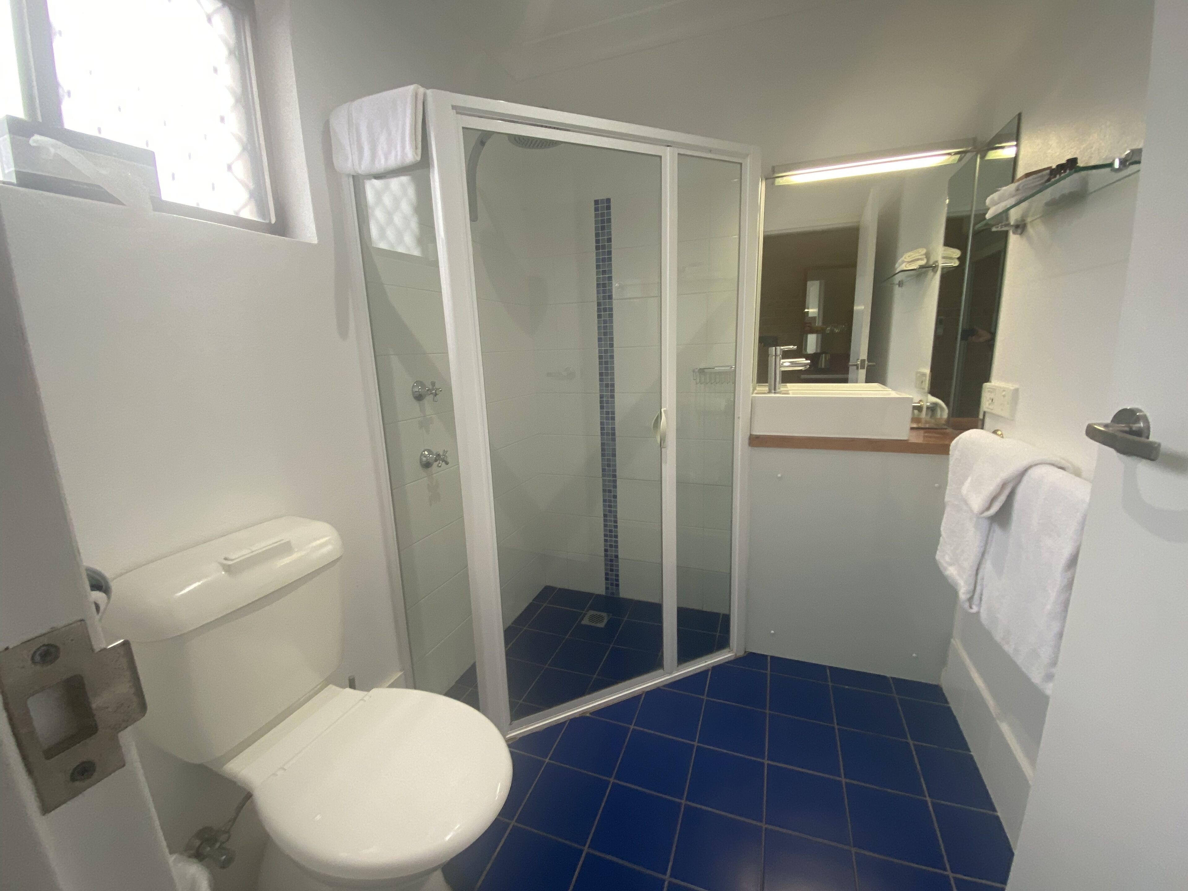 Un baño con inodoro, ducha con mampara de vidrio y lavamanos con espejo.