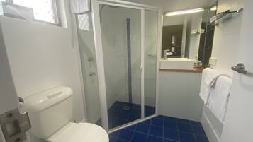 Un baño con inodoro, ducha con mampara de vidrio y lavamanos con espejo.
