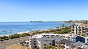 Une vue sur la côte, avec des bâtiments modernes, un ciel bleu dégagé et une plage au loin.