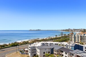 A coastal view with modern buildings, a clear blue sky, and a beach in the distance.
