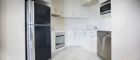 A modern kitchen with white cabinets, a stainless steel refrigerator, an oven, a dishwasher, and a microwave.