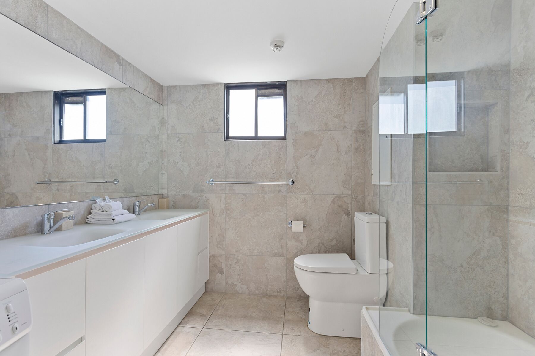 A modern bathroom with a glass-enclosed shower, a toilet, and a vanity with a sink and towel rack.