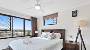 Une chambre d’hôtel avec un grand lit, un ventilateur de plafond, une table de chevet avec une lampe, une décoration en forme d’étoile et une citation inspirante sur le mur.