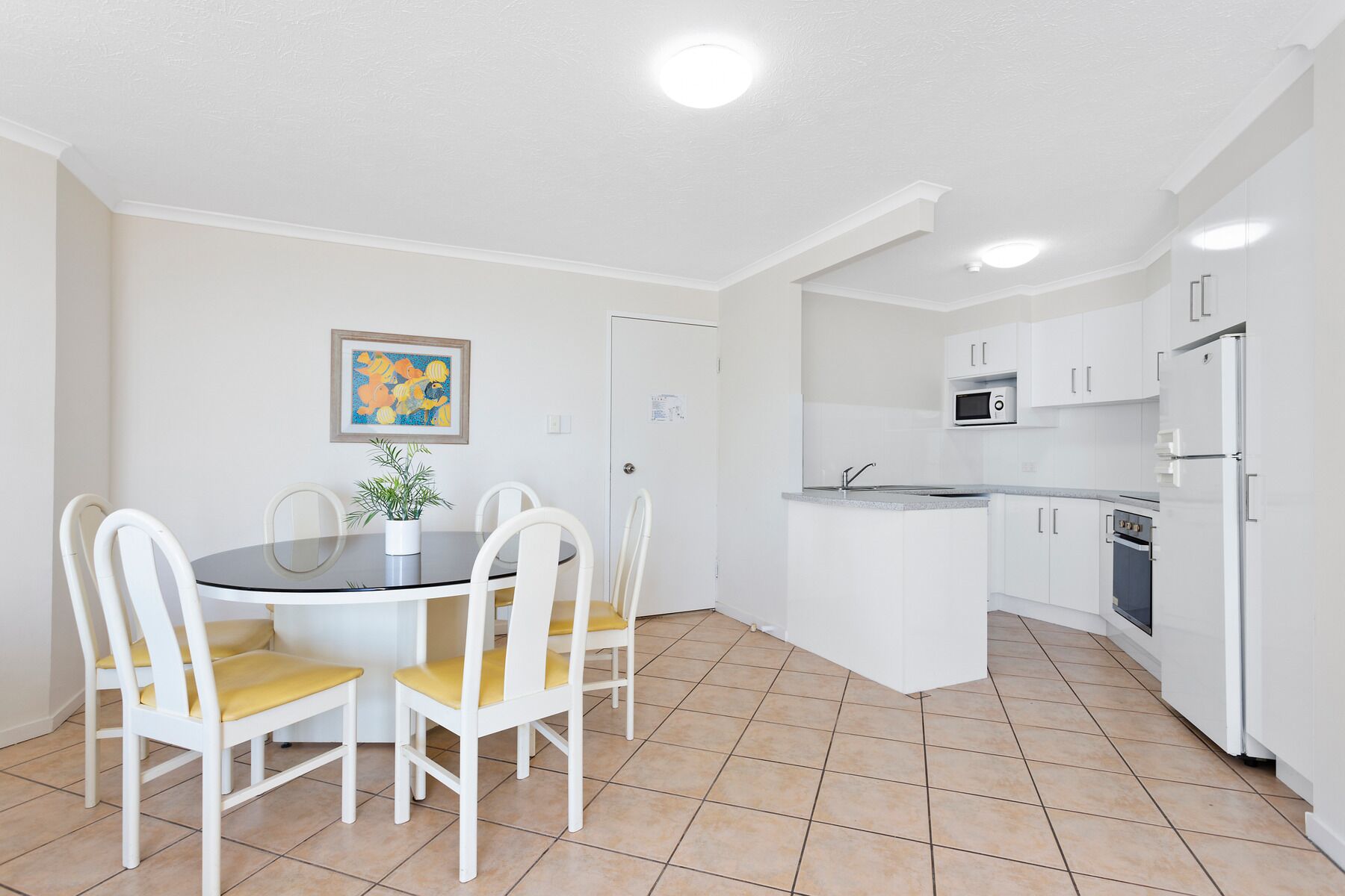 Una cocina compacta con armarios blancos, un microondas y un refrigerador.