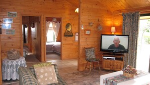 Un interior de cabaña acogedor con televisión, sofá, sillón y cama.