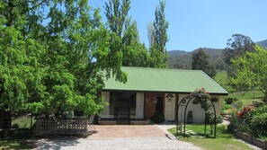 A small, single-story building with a green roof, surrounded by lush greenery and a gravel driveway. - Edelweiss Cottage B&B (Dederang)