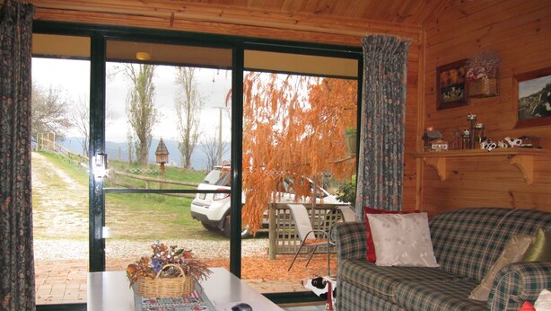 Un interior de cabaña acogedor con un sofá de cuadros, una mesa de centro con un camino decorativo, y vista a un coche estacionado afuera.