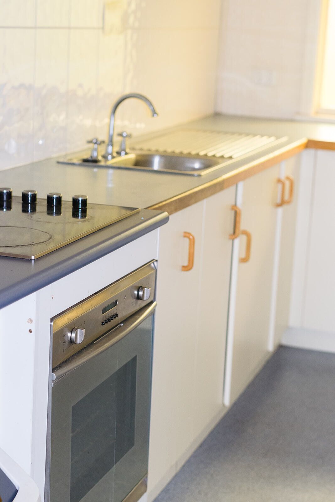 Cucina con piano cottura, forno, lavello e mobili bianchi.