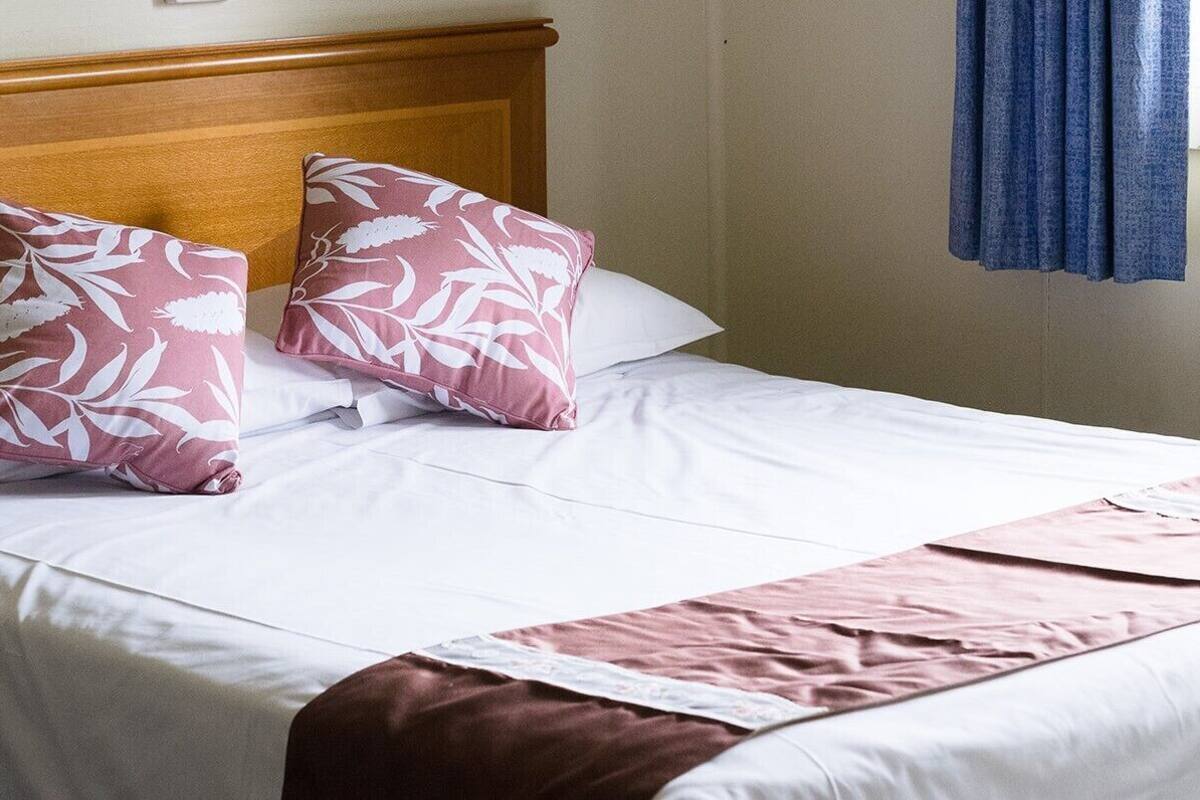 Una cama bien hecha con almohadillas florales blancos y rosas, un cabecero de madera y una cortina azul.