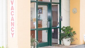 A building entrance with a 'VACANCY' sign, a green door, and potted plants. - Echuca Motel (Echuca)
