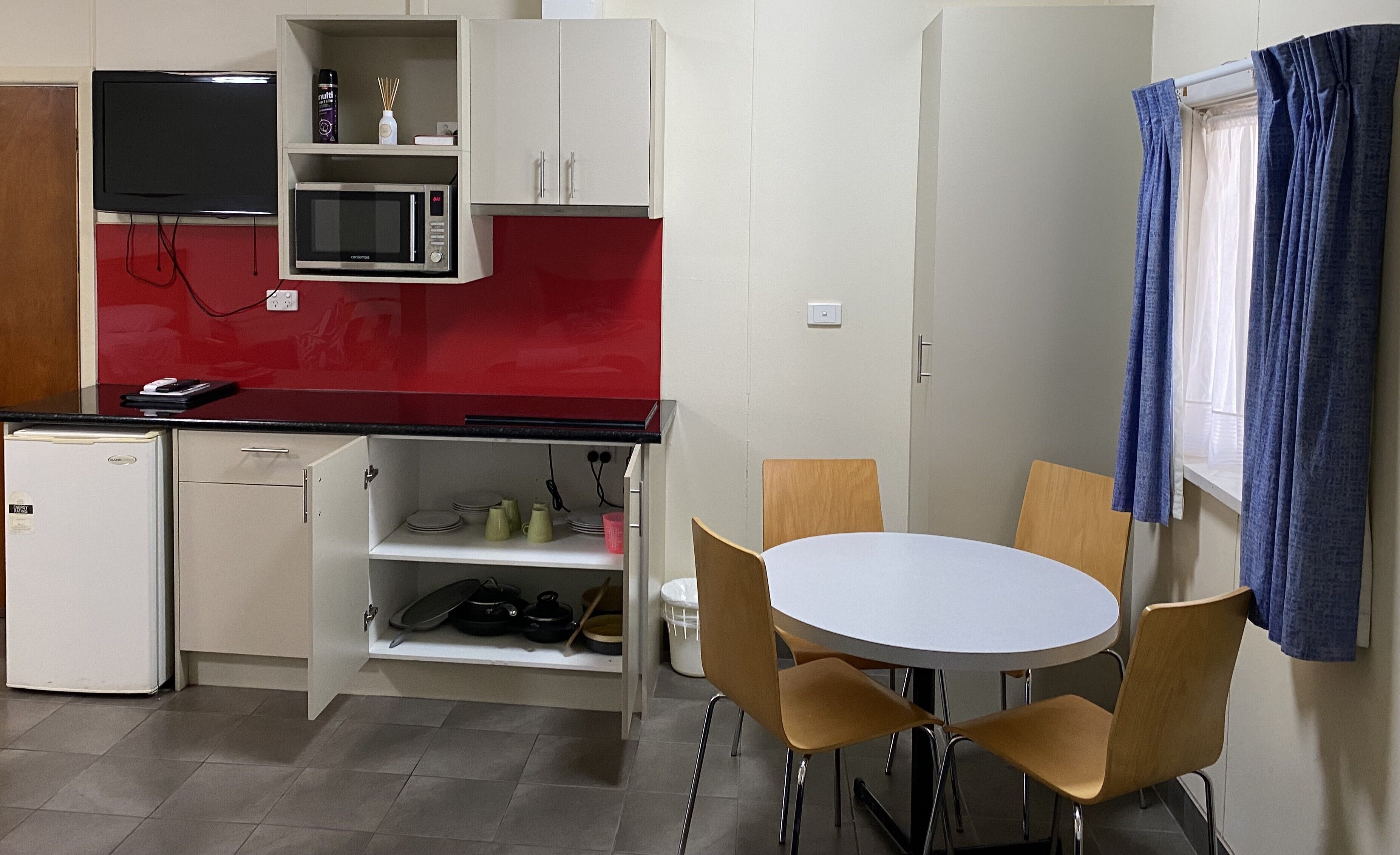 Una cocina compacta con microondas, un refrigerador pequeño y un comedor con mesa y sillas.