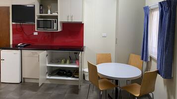 Una cocina compacta con microondas, un refrigerador pequeño y un comedor con mesa y sillas.