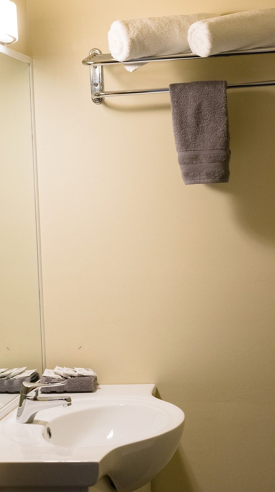 A bathroom with a white sink, a mirror, and a towel rack with two towels.