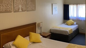 A hotel room with two beds, each with yellow pillows, a wooden headboard, a bedside table with a lamp, and artwork on the wall. - Echuca Motel (Echuca)