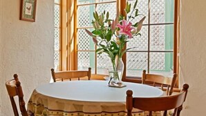 Una mesa redonda de comedor con mantel blanco, rodeada de sillas de madera. Un jarrón con flores rosadas está sobre la mesa.