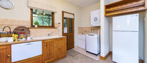A kitchen with wooden cabinets, a white refrigerator, a sink, and a window with a view of greenery.