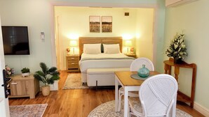 A cozy bedroom with a bed, bedside lamps, a TV, a small table with a vase, and a chair. - Curtis Falls Apartment (Tamborine Mountain)