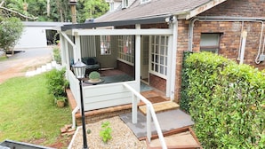 A covered porch with a seating area, a small table, and a potted plant. - Curtis Falls Apartment (Tamborine Mountain)
