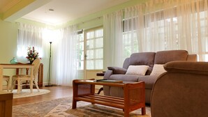 A living room with a sofa, a coffee table, a chair, and a table with a vase of flowers. - Curtis Falls Apartment (Tamborine Mountain)